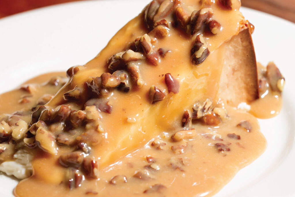 A slice of cheesecake topped with pecans and caramel-colored sauce